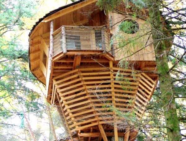 Cabane dans les arbres avec un balcon en bois, nichée parmi les feuillages.