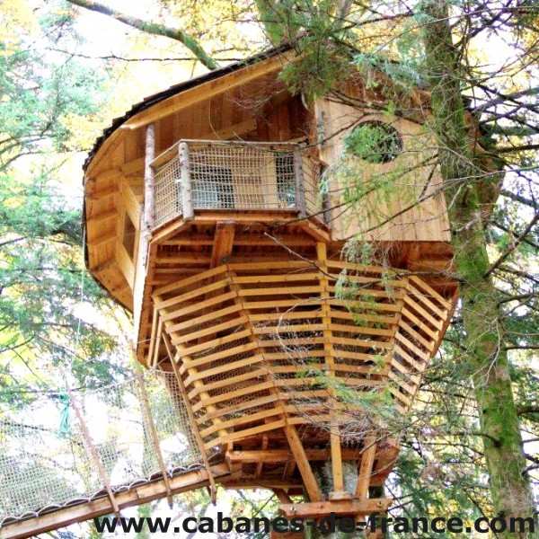 Cabane dans les arbres avec un balcon en bois, nichée parmi les feuillages.