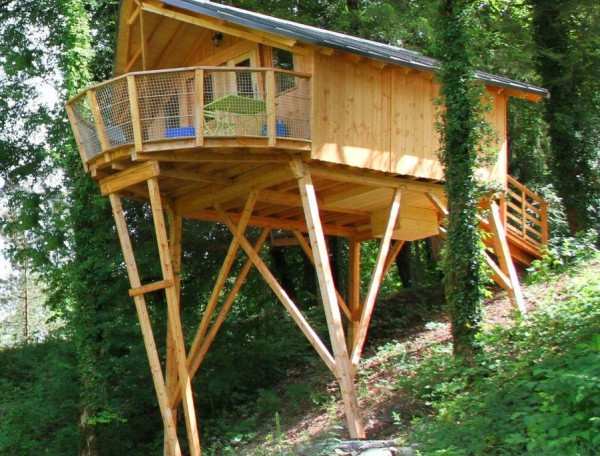 Cabane perchée en bois, entourée darbres, offrant une vue imprenable sur la nature.