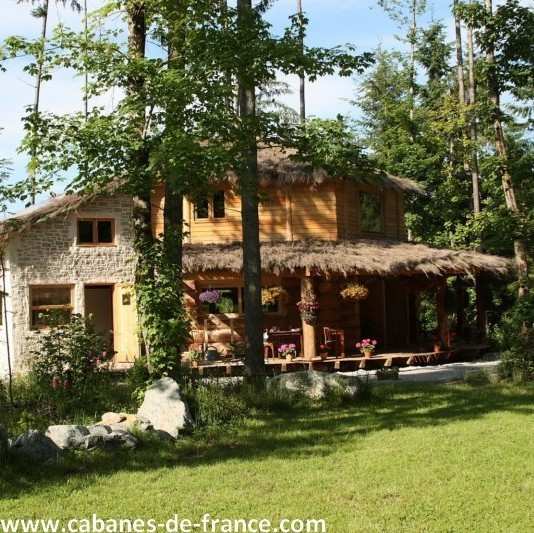 Charmante cabane en bois avec toit de chaume, entourée de verdure luxuriante.