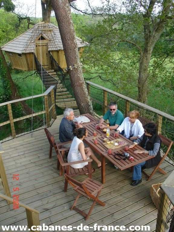 1497 Cabane dans les arbres en Bretagne, avec une terrasse en bois et des convives autour dune table.