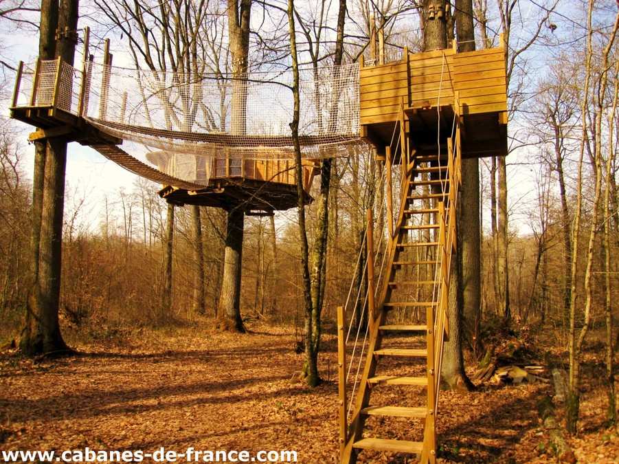 Cabane dans les arbres à Champagne-Ardenne, perchée et accessible par un escalier en bois.