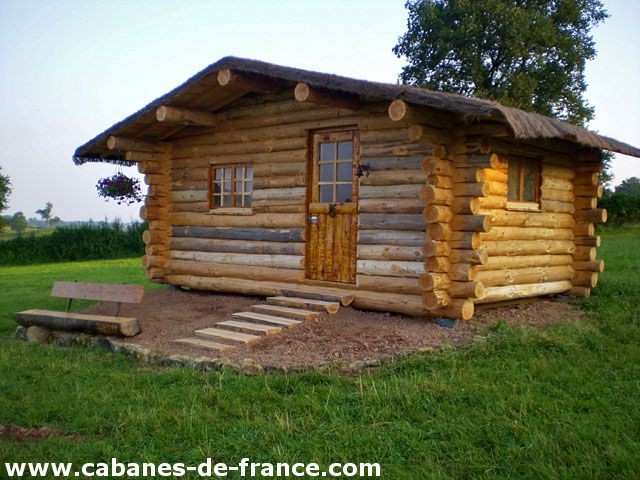 Cabane en bois dans la nature, avec un toit en chaume et une terrasse accueillante.