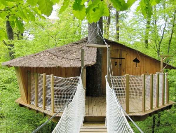 Cabane perchée dans les arbres, accessible par un pont suspendu, au cœur de la nature.