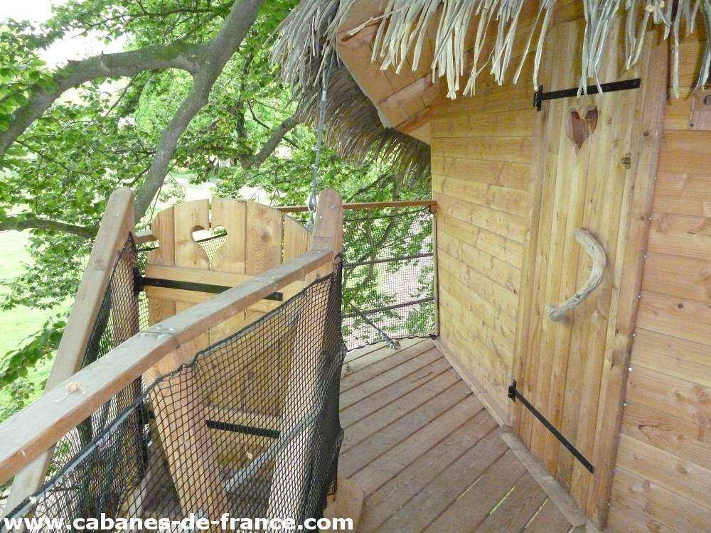 2054 Cabane perchée en bois avec balustrade, entourée darbres verdoyants.