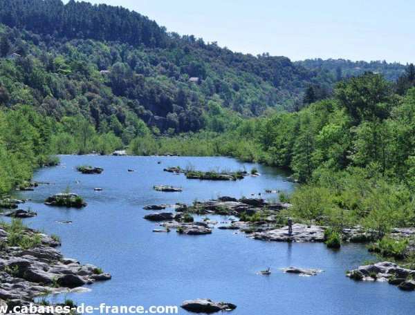 Cabane en bois au bord dune rivière, entourée de verdure luxuriante.