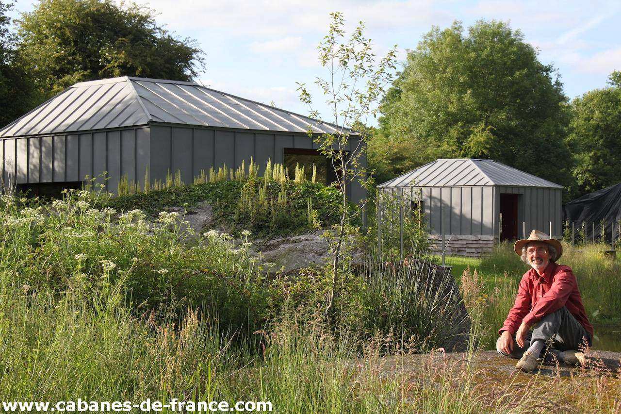 2174 Cabane moderne en pleine nature, entourée de verdure et dun homme souriant.