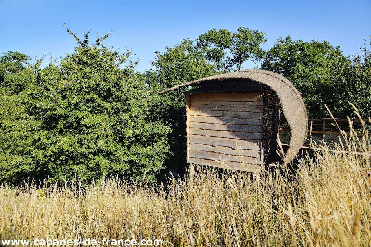 2191 Cabane en bois au milieu des champs, avec un toit courbé et verdure environnante.