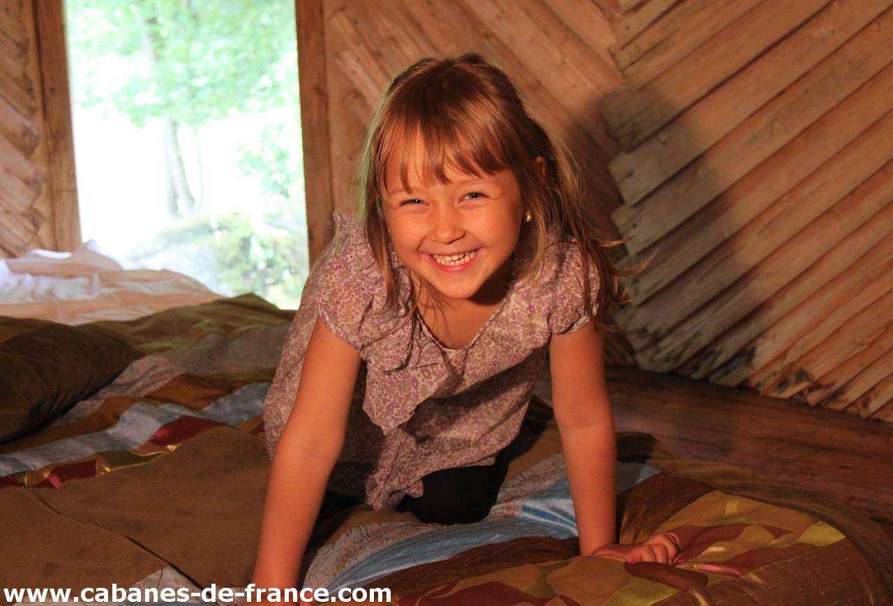 2201 Cabane en bois dans les Pays de la Loire, avec une petite fille souriante sur un lit coloré.