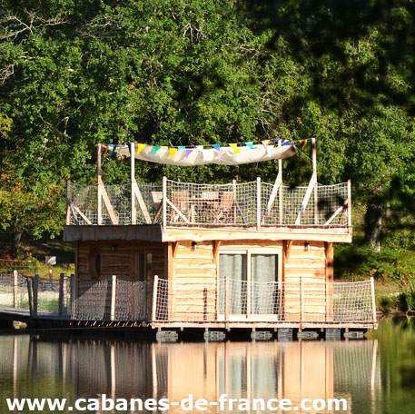 Cabane flottante en bois avec terrasse surplombant un lac paisible.