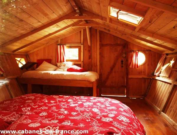Cabane en bois en Bretagne, intérieur chaleureux avec lits douillets et fenêtres rondes.