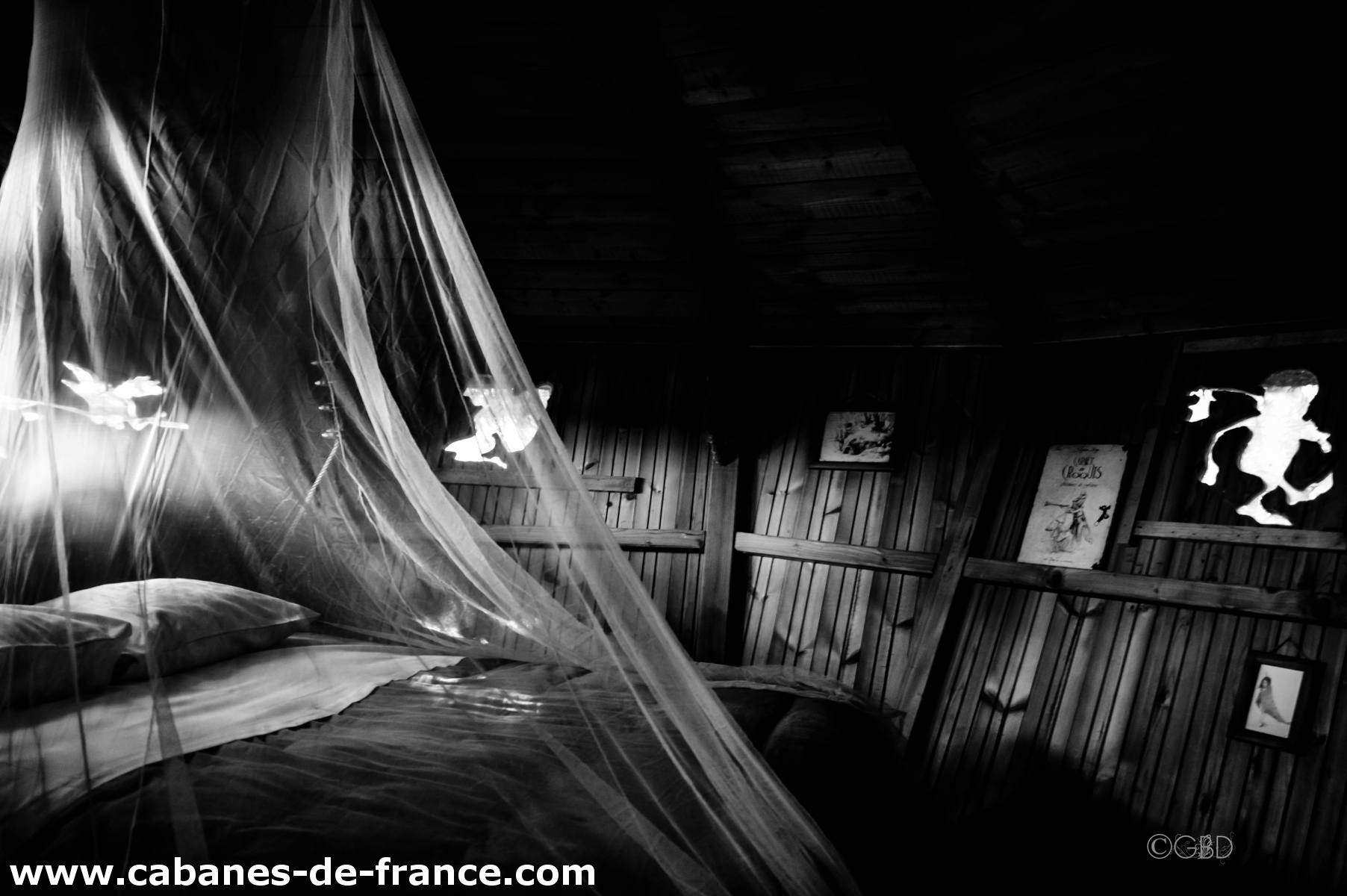 3071 Cabane en bois en Bretagne, lit sous un voile délicat et décor mural artistique.