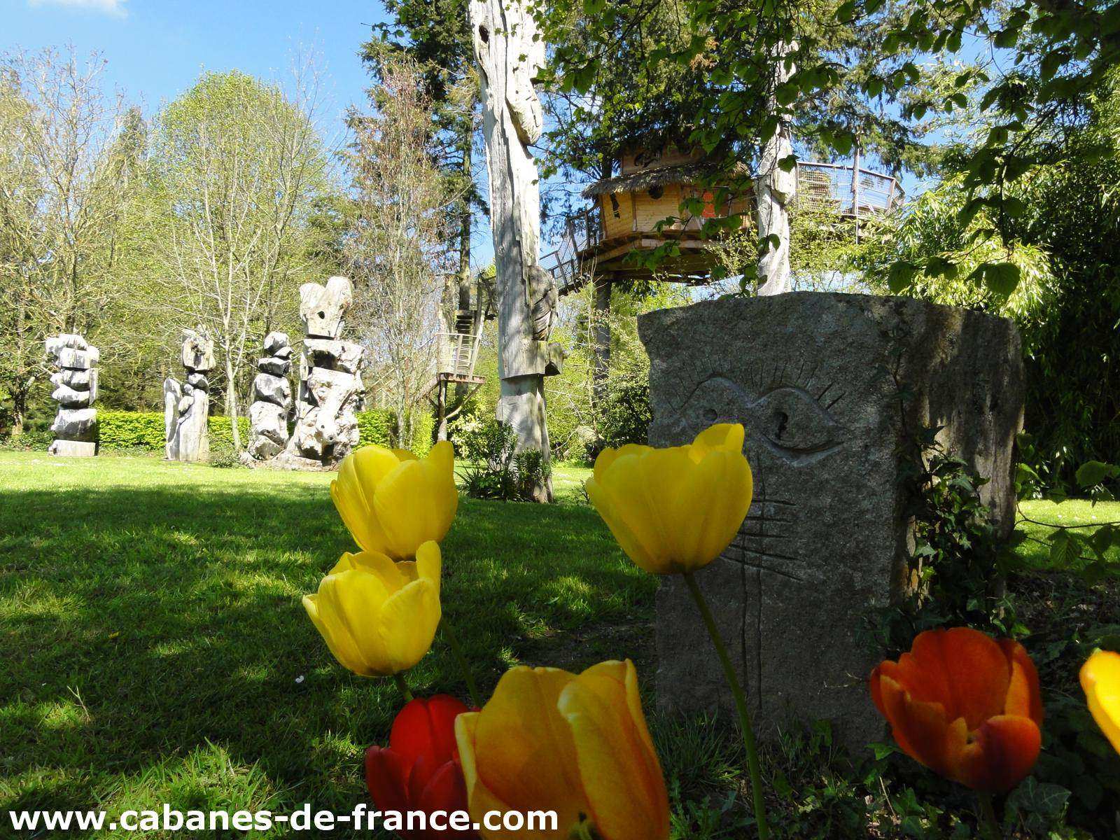 3097 Cabane perchée en Bretagne, entourée de sculptures et de fleurs colorées.