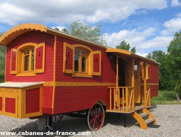 Charmante roulotte rouge avec fenêtres jaunes, entourée de verdure.