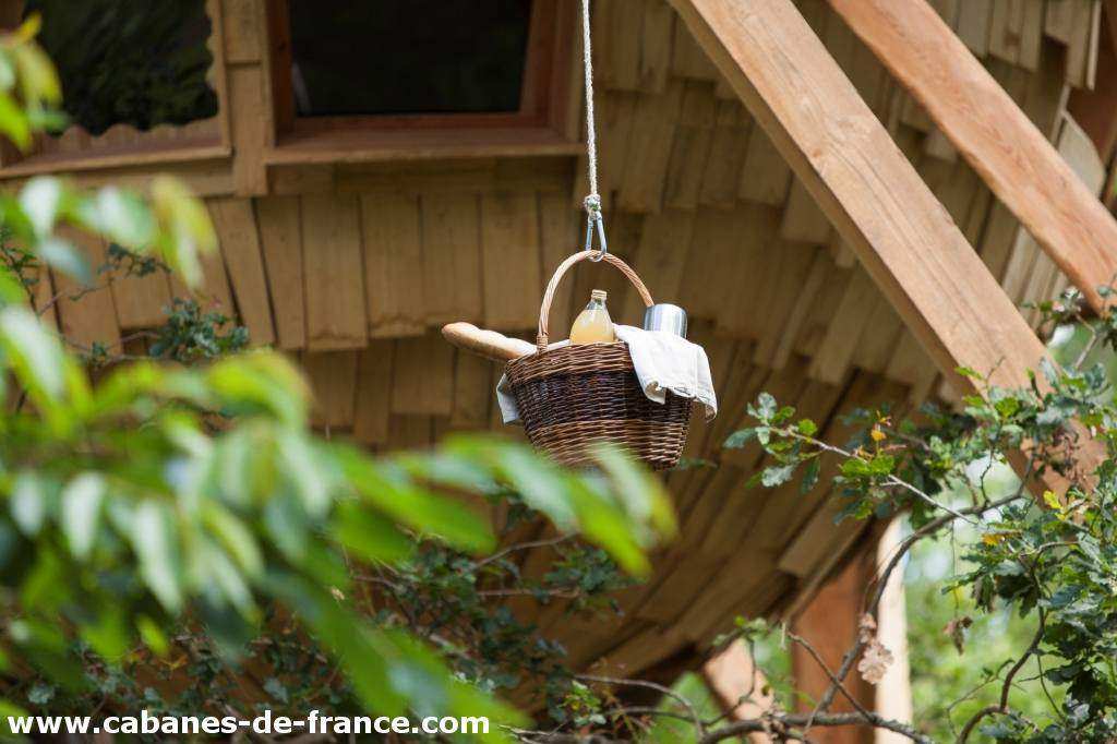 3414 Cabane perchée dans les arbres, panier suspendu avec des douceurs à lentrée.