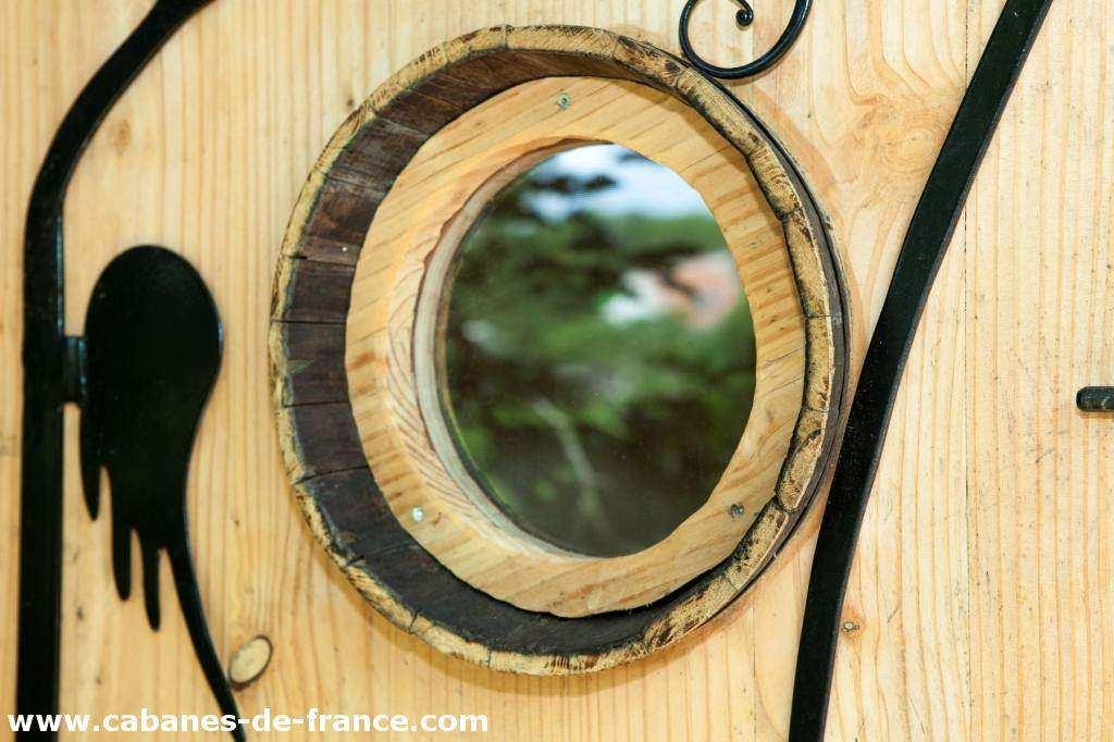 3419 Cabane en bois avec un miroir rond encastré dans la porte, ambiance naturelle.