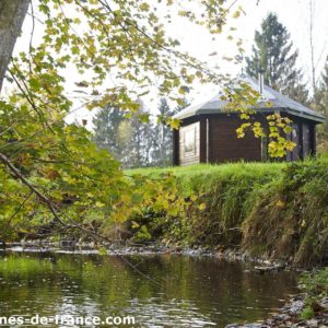 Cabane en bois au bord dun ruisseau, entourée darbres verdoyants.