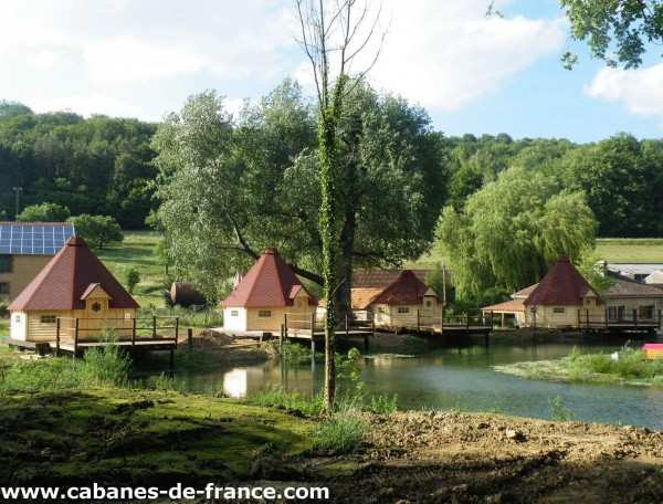 Cabanes en bois au bord dun étang, entourées de verdure et de nature paisible.