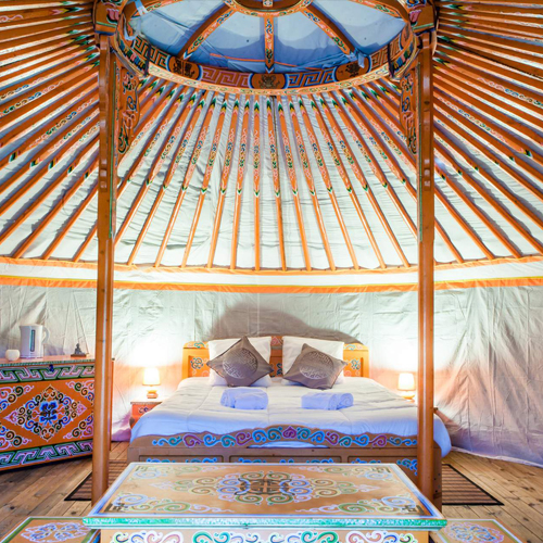 CC-Nomade-photo2 Yourte colorée avec un lit douillet et des décorations artisanales.