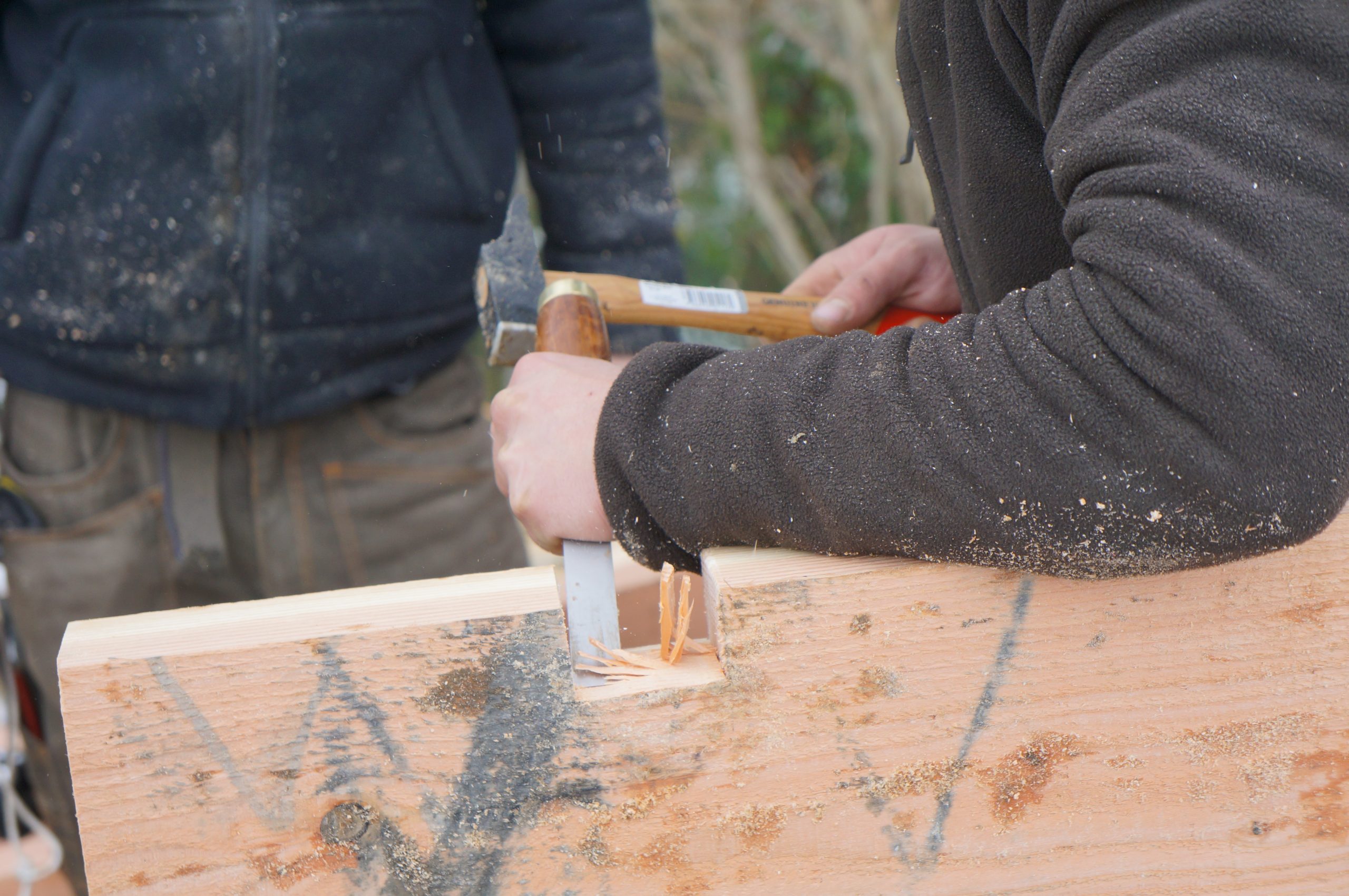 Hébergement en bois, artisan au travail sur une pièce de bois, ambiance chaleureuse.