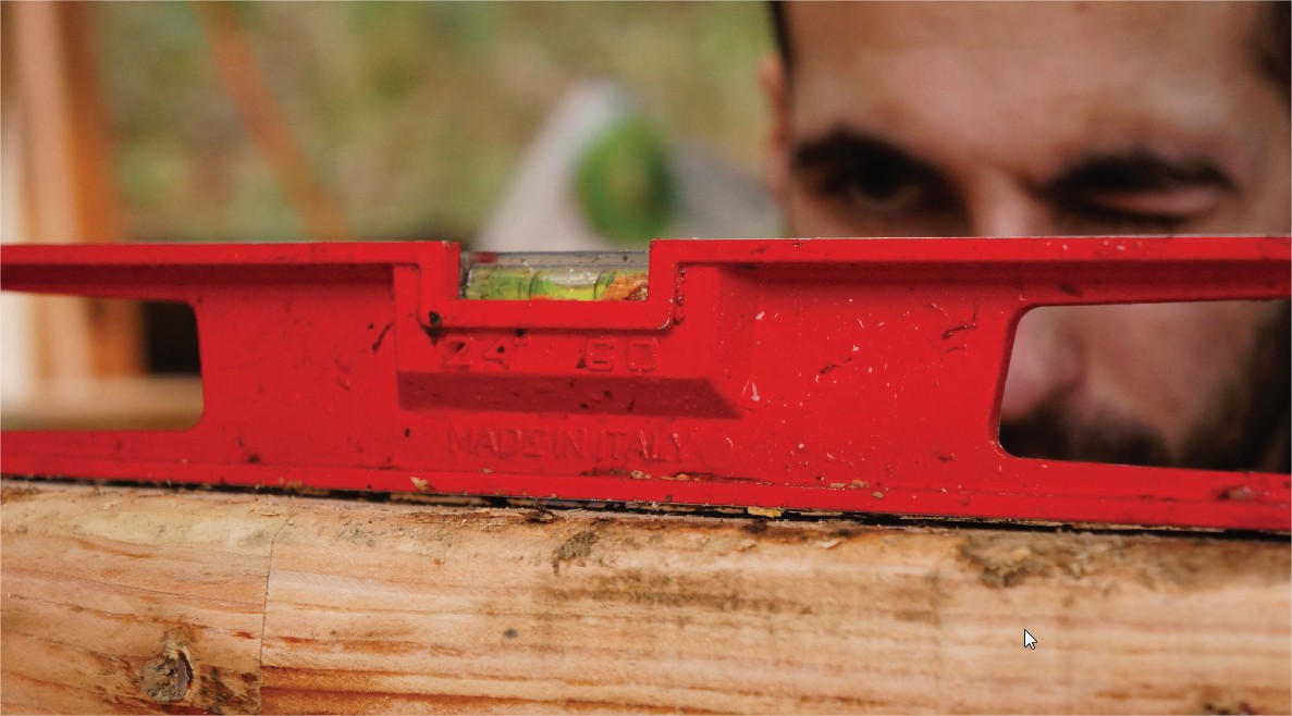 Hébergement en bois, un artisan vérifie lhorizontalité avec un niveau rouge.