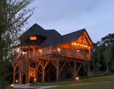 Cabane dans les arbres illuminée, entourée de verdure et dune ambiance paisible.