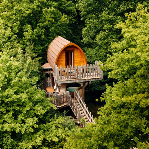 CC-Escapade-photo2 Cabane perchée en bois, entourée darbres verdoyants et avec une terrasse accueillante.
