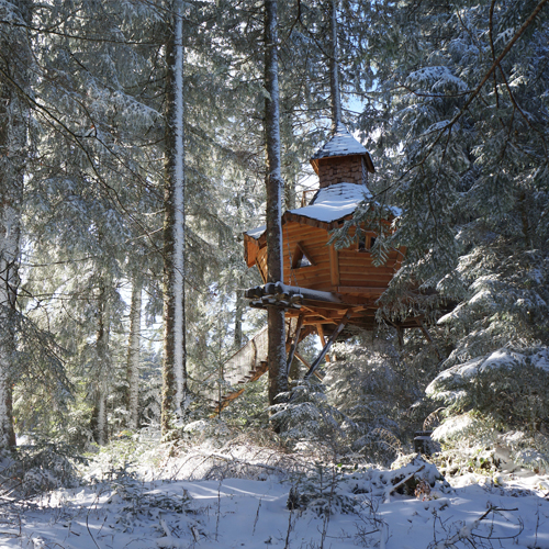 CC-Escapade-photo4 Cabane dans les arbres en bois, entourée de neige et de sapins majestueux.