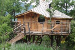 Cabane dans les arbres en bois, perchée au milieu de la verdure luxuriante.