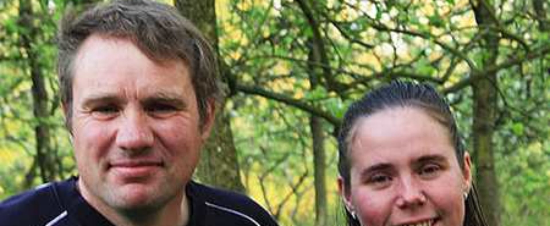 Couple souriant devant un gîte rural, entouré darbres verdoyants.