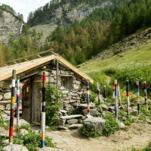 Chalet en pierre entouré de poteaux colorés, niché dans une vallée verdoyante.