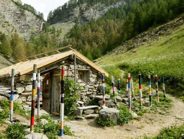 Chalet en pierre entouré de poteaux colorés, niché dans une vallée verdoyante.