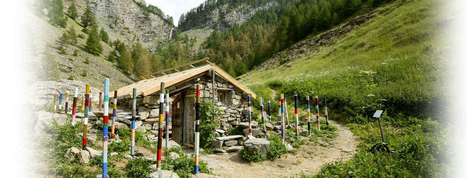Chalet en pierre entouré de poteaux colorés, niché dans une vallée verdoyante.
