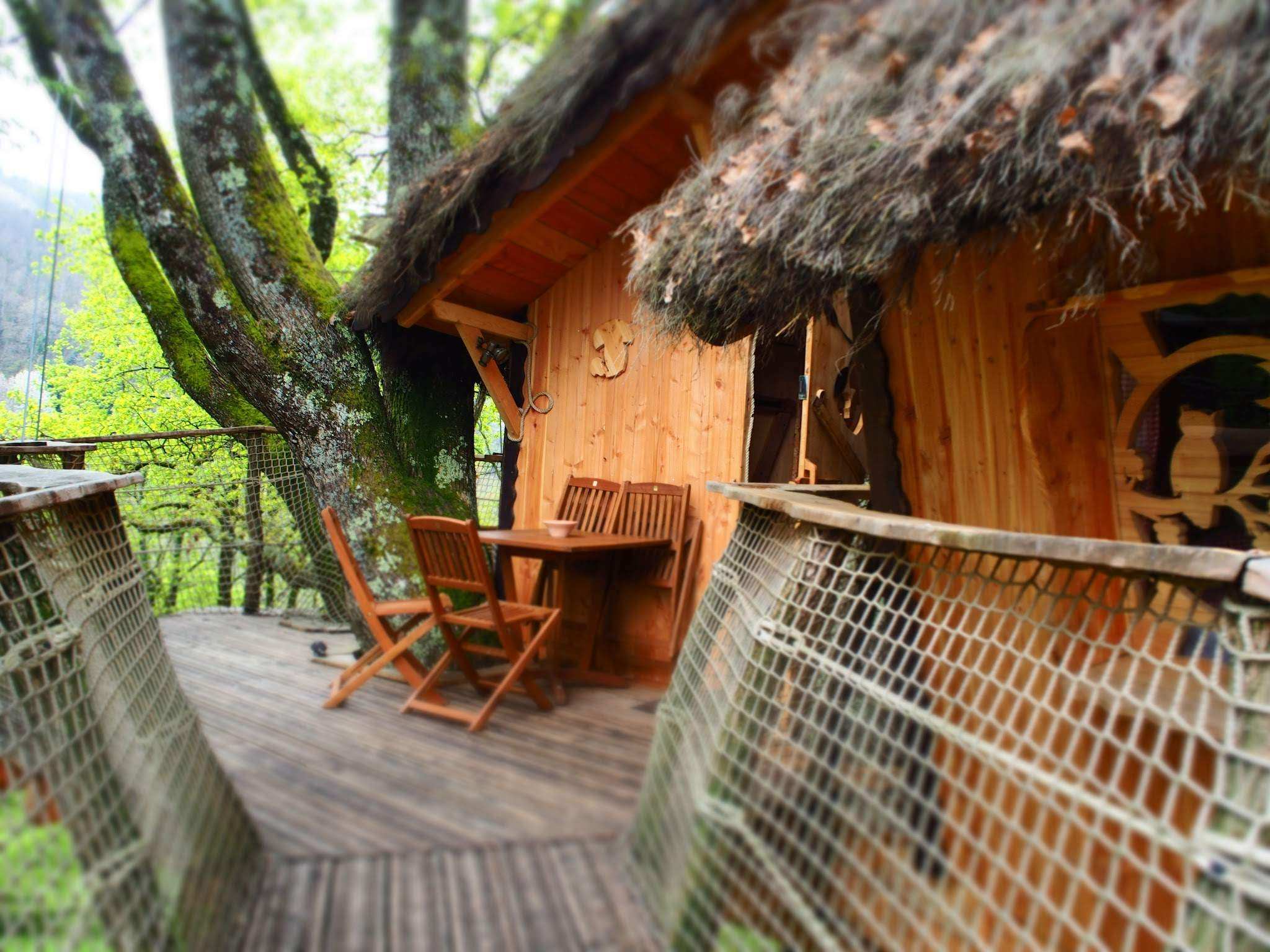 4289 Cabane perchée en bois avec terrasse en bois, entourée darbres verdoyants.