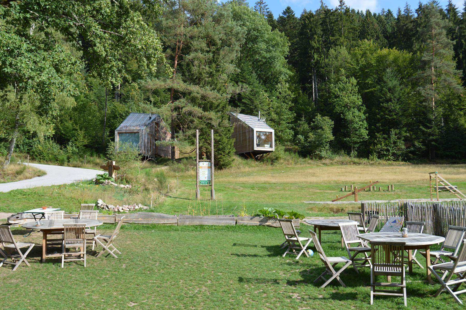 Hébergement insolite en cabanes dans les arbres, entouré de verdure et de mobilier en bois.