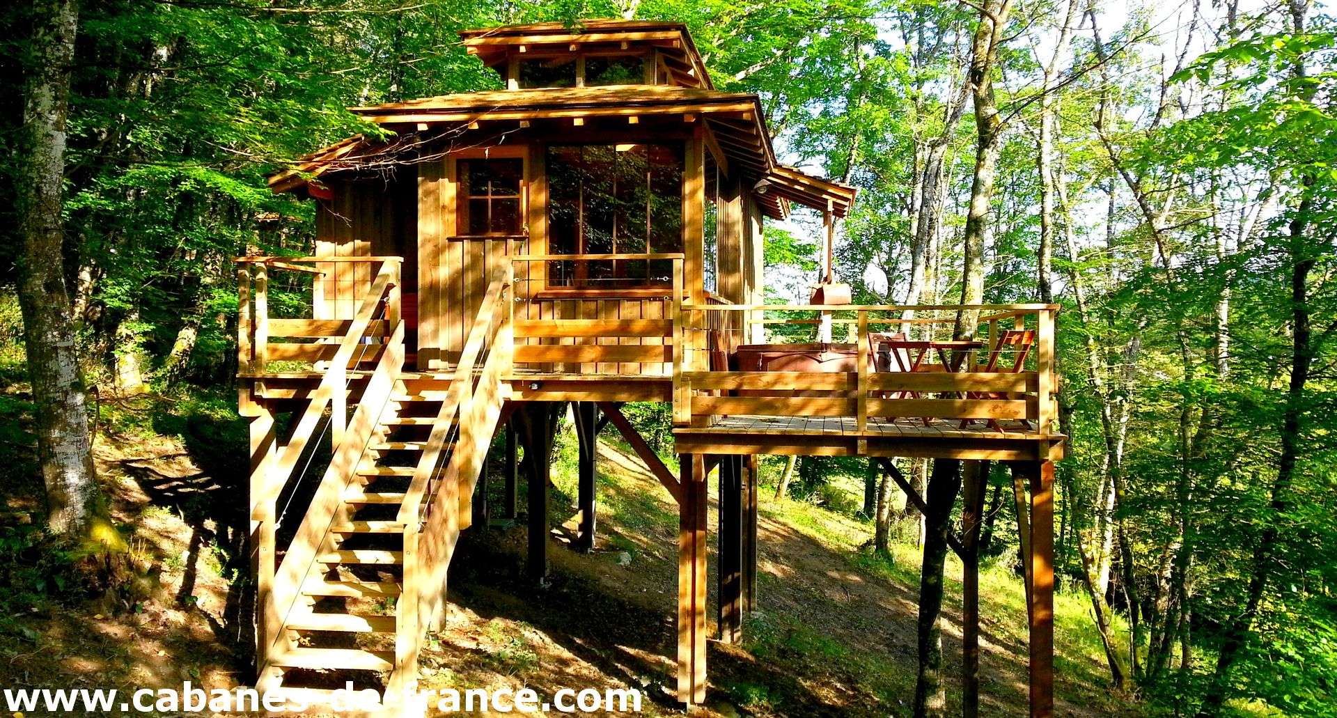 Cabane dans les arbres en bois, perchée sur pilotis, entourée de verdure.