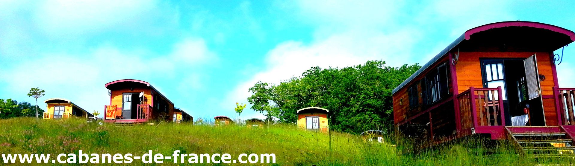 Charmantes cabanes en bois colorées, entourées de verdure sous un ciel bleu.