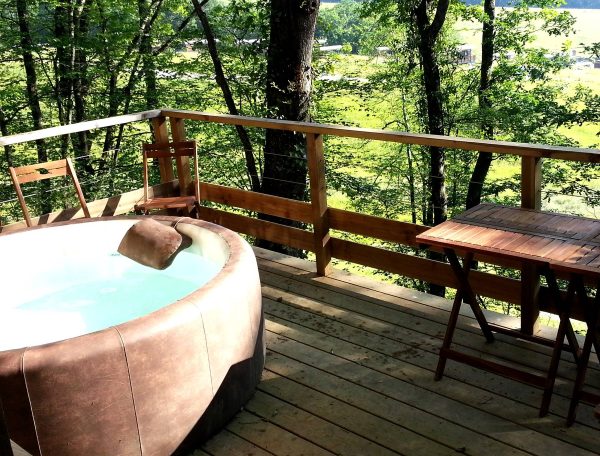 Cabane en bois avec jacuzzi sur une terrasse entourée darbres verdoyants.