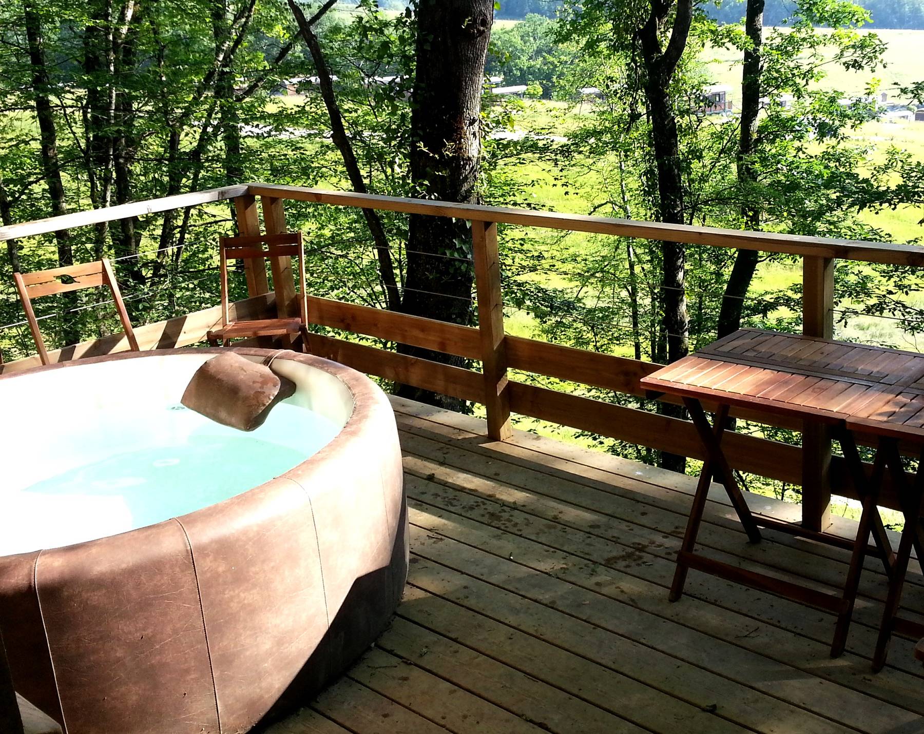 Cabane en bois avec jacuzzi sur une terrasse entourée darbres verdoyants.