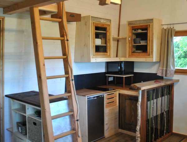 Cabane en bois avec mezzanine, cuisine équipée et échelle en bois.