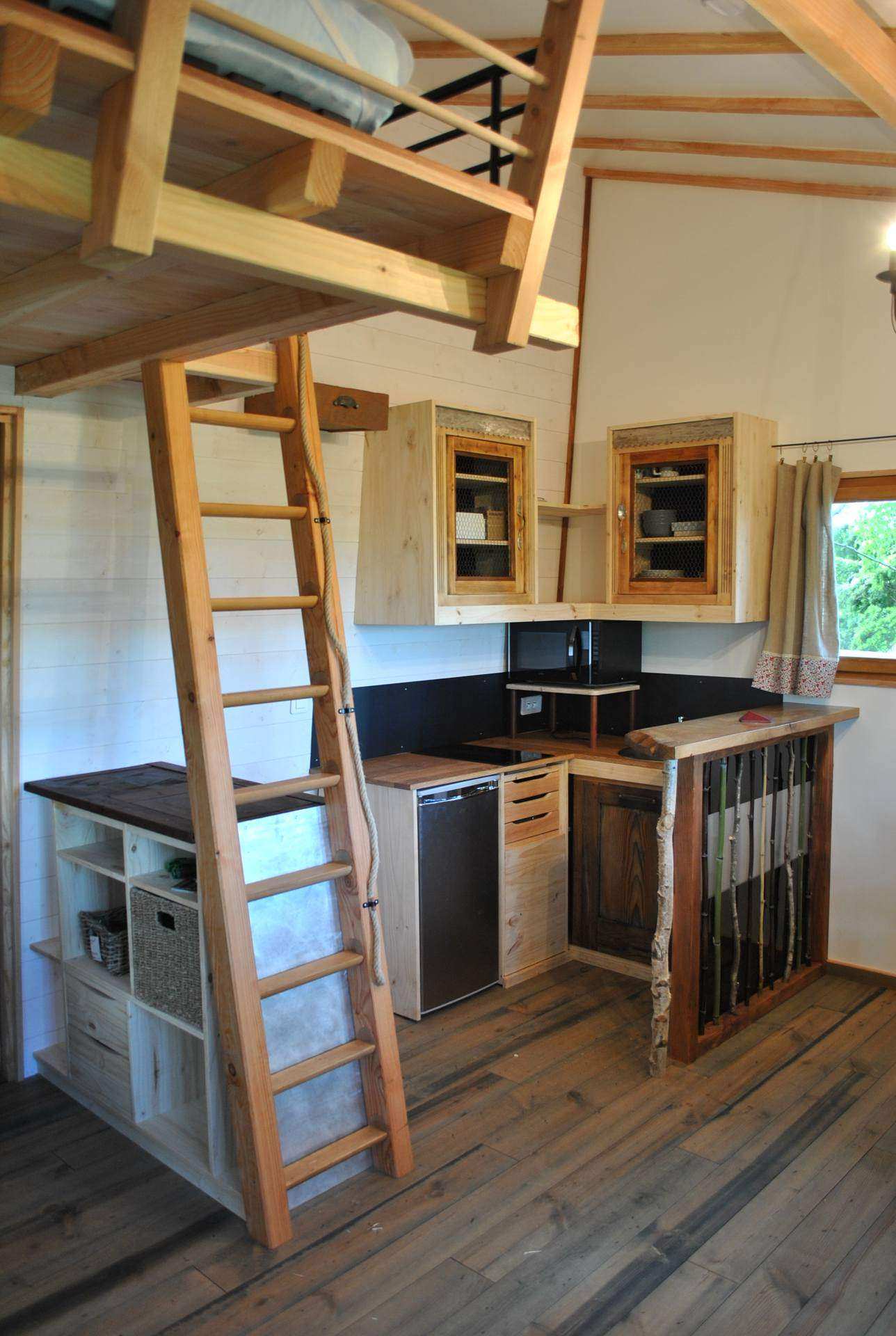 Cabane en bois avec mezzanine, cuisine équipée et échelle en bois.