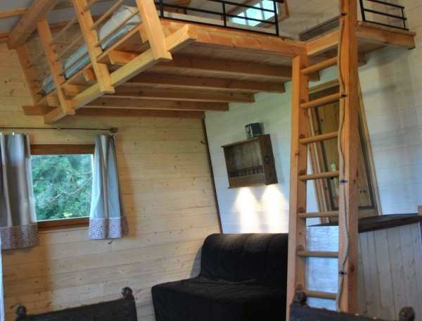 Chalet en bois avec mezzanine, intérieur chaleureux et mobilier en bois.