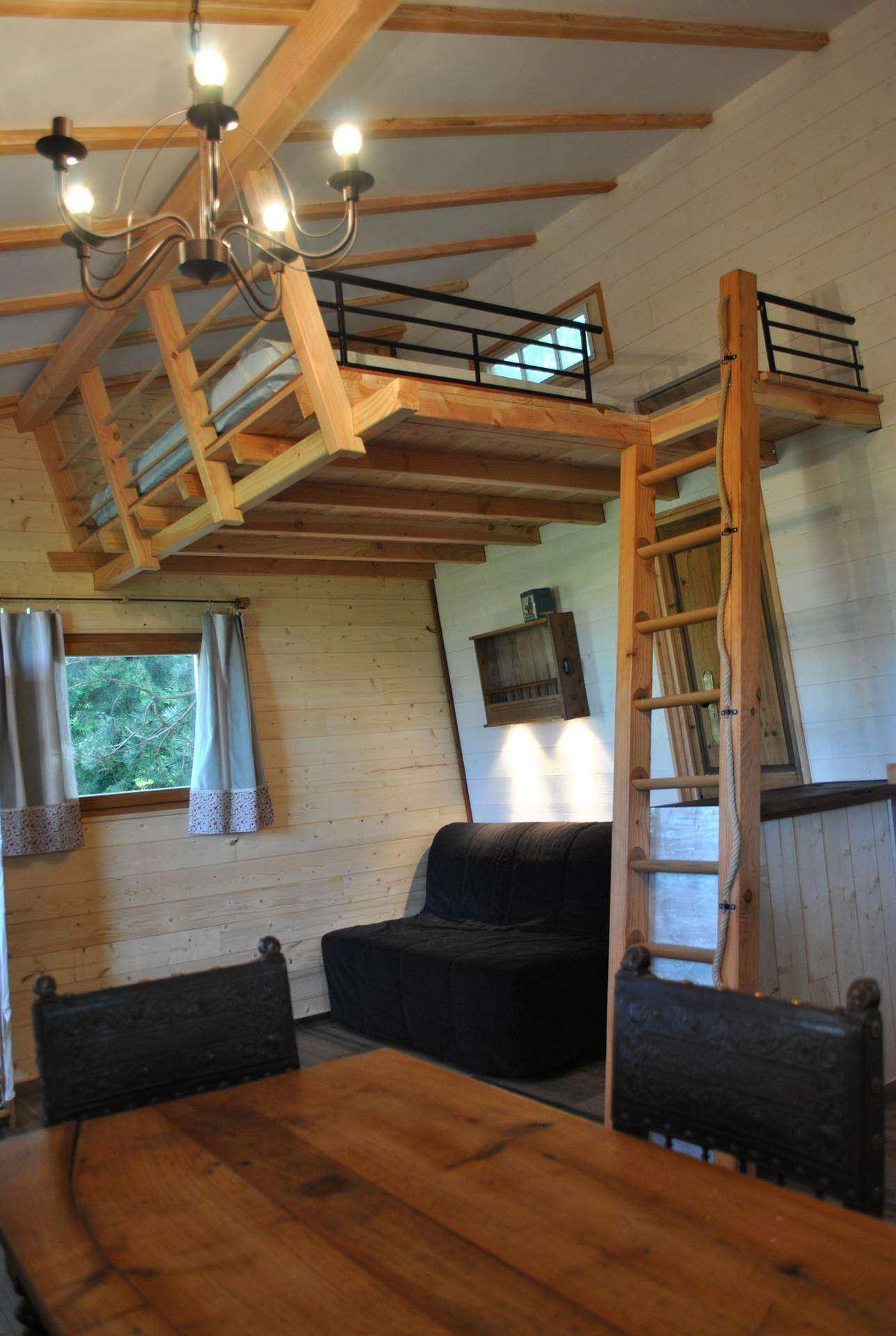 Chalet en bois avec mezzanine, intérieur chaleureux et mobilier en bois.