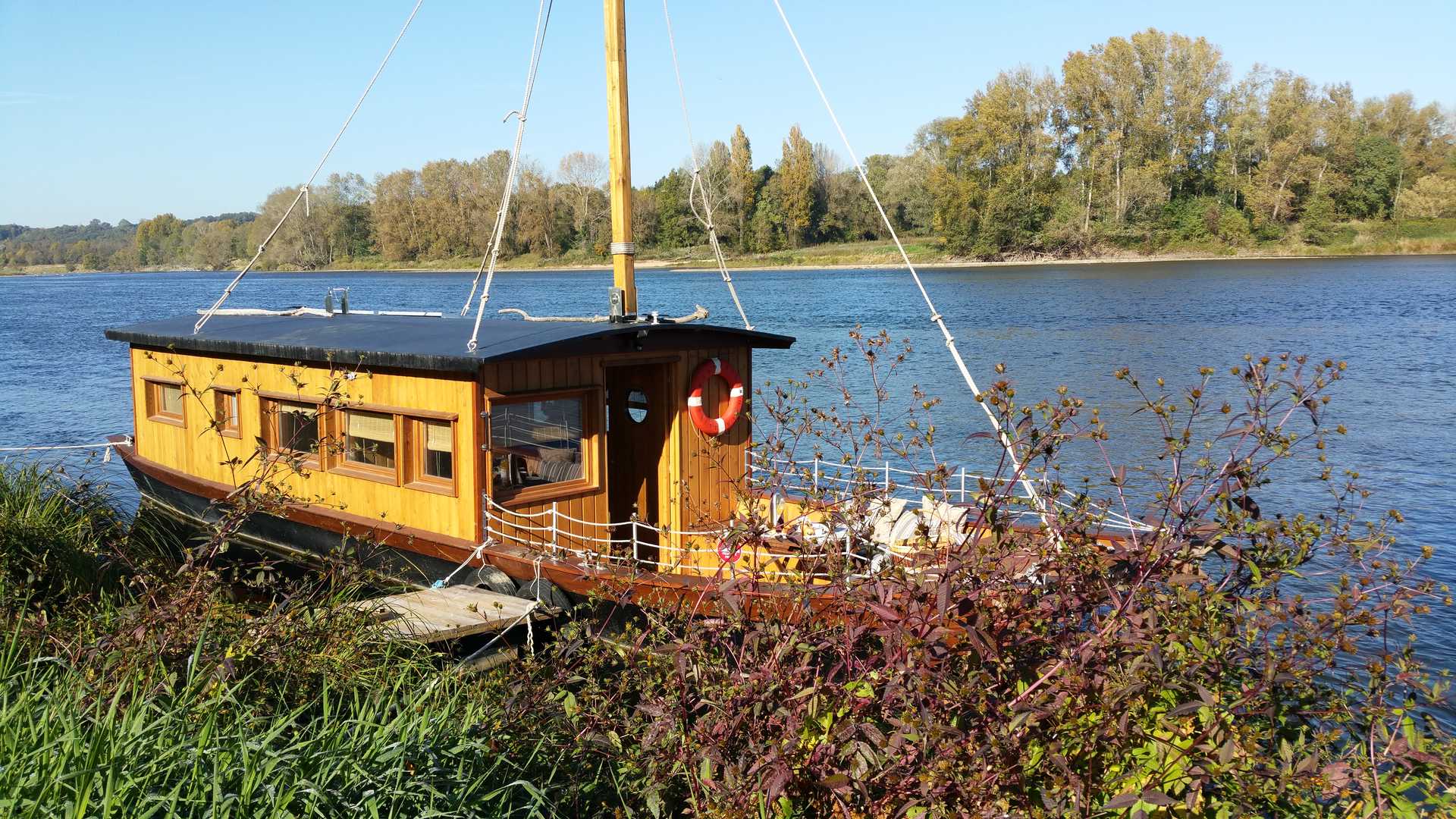 20151019_114922 Hébergement insolite : une péniche en bois amarrée au bord de la rivière, entourée de verdure.