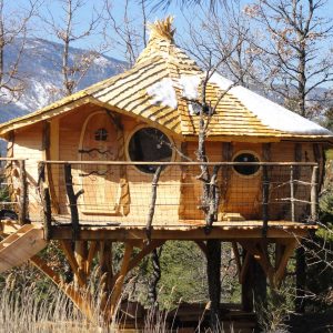 Cabane perchée en bois avec un toit en bardeaux et balustrade en bois.