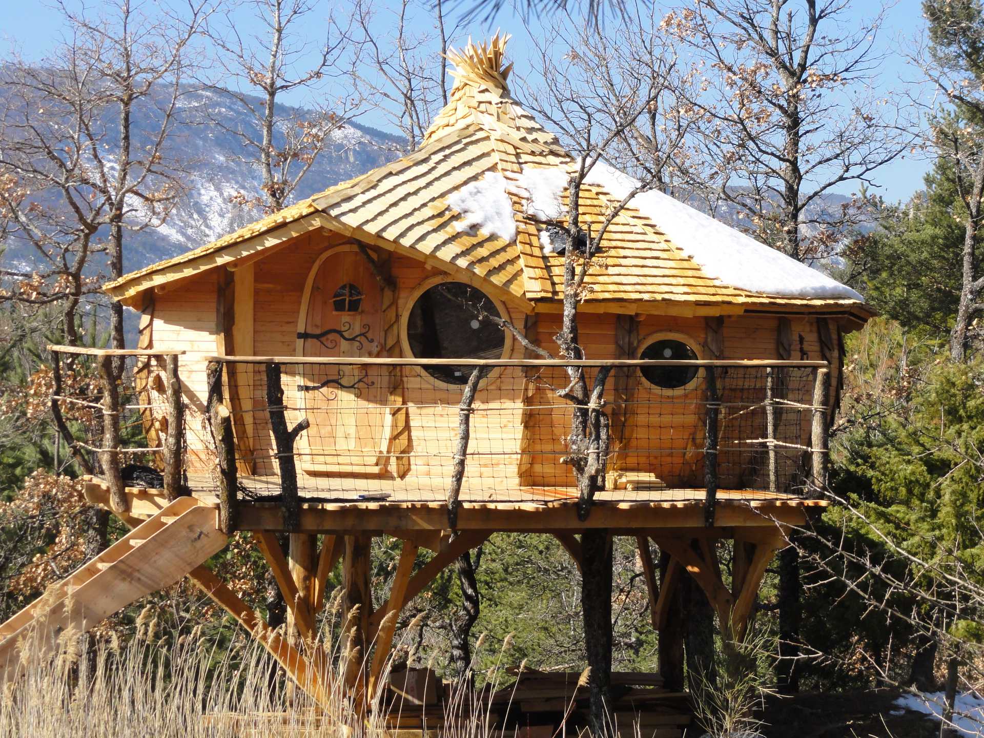 Cabane perchée en bois avec un toit en bardeaux et balustrade en bois.