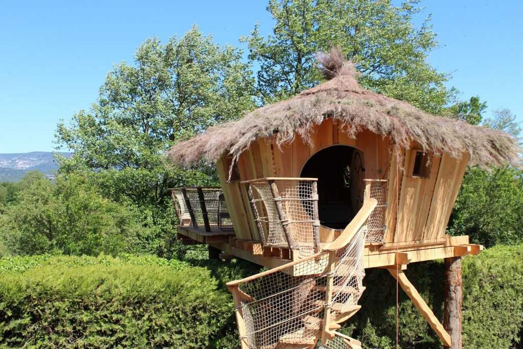 Cabane perchée en bois avec toit en chaume, entourée de verdure en Provence.