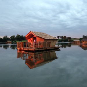 Cabane flottante sur un lac, avec une terrasse en bois et un reflet paisible.