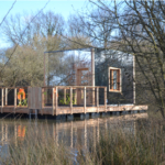 Cabane flottante sur un étang, entourée de verdure et de calme.