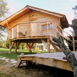 Cabane en bois sur pilotis avec terrasse ensoleillée et vue sur la nature environnante.